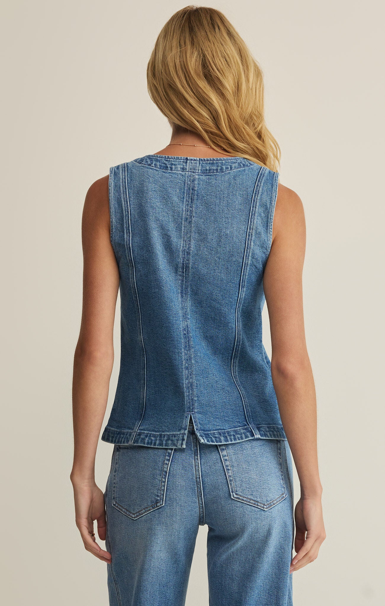 Person wearing a blue denim vest and jeans on a beige background