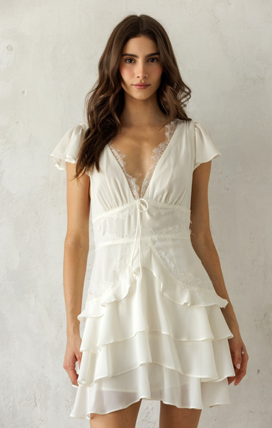 Woman wearing a white dress with ruffled layers against a plain background