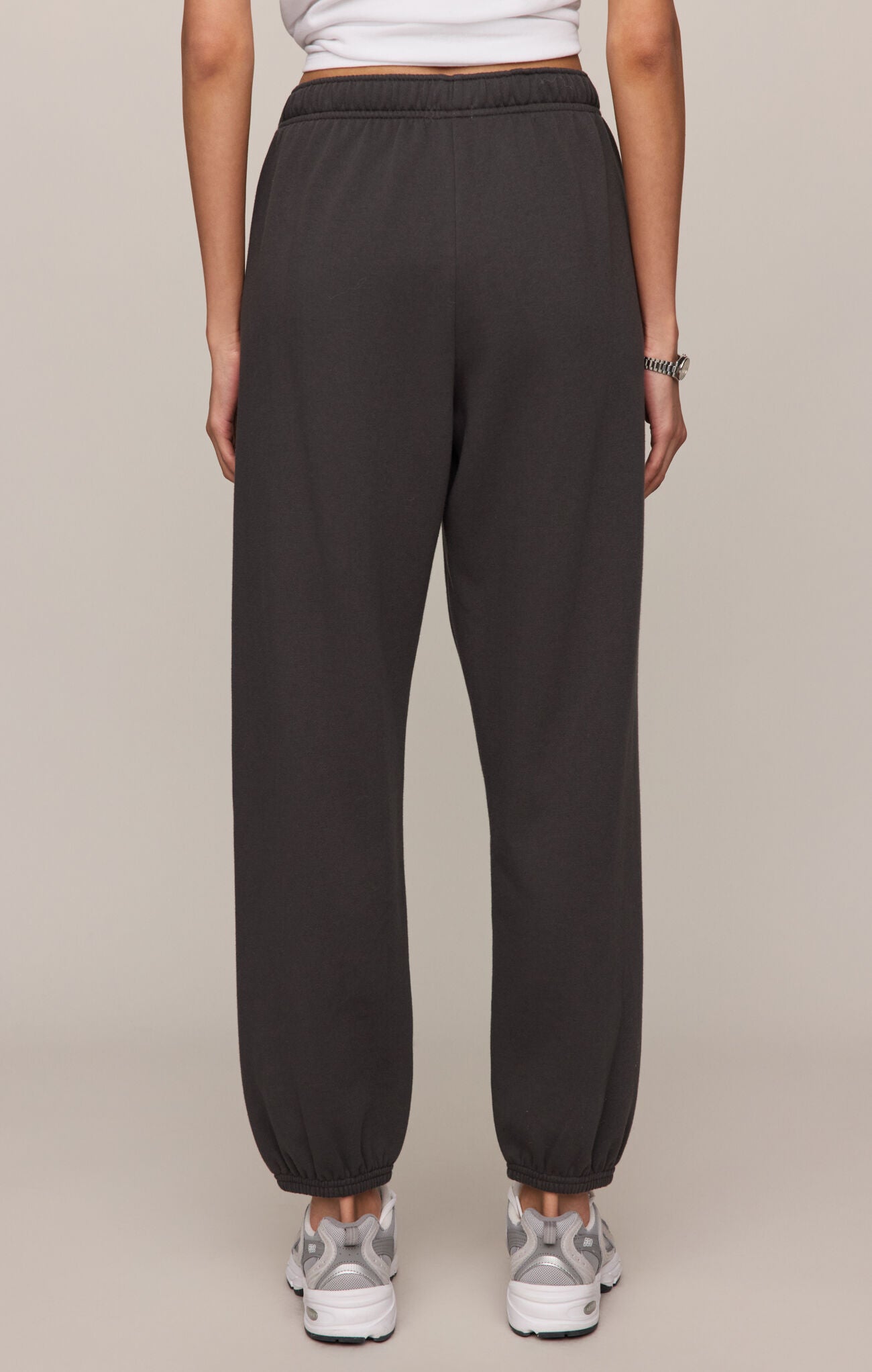Person wearing dark gray sweatpants on a beige background
