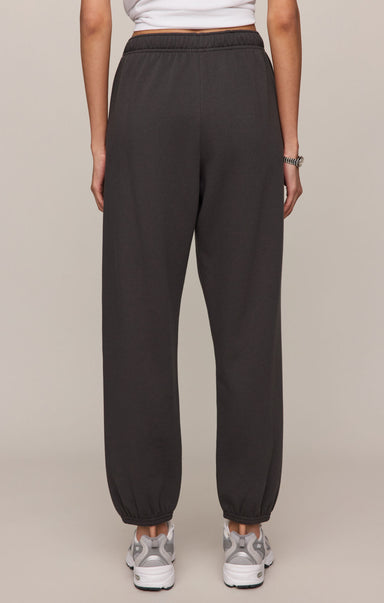 Person wearing dark gray sweatpants on a beige background
