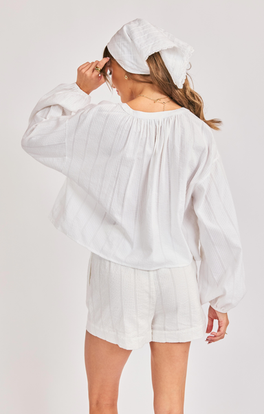 Person wearing a white blouse and shorts with a white headscarf on a light gray background