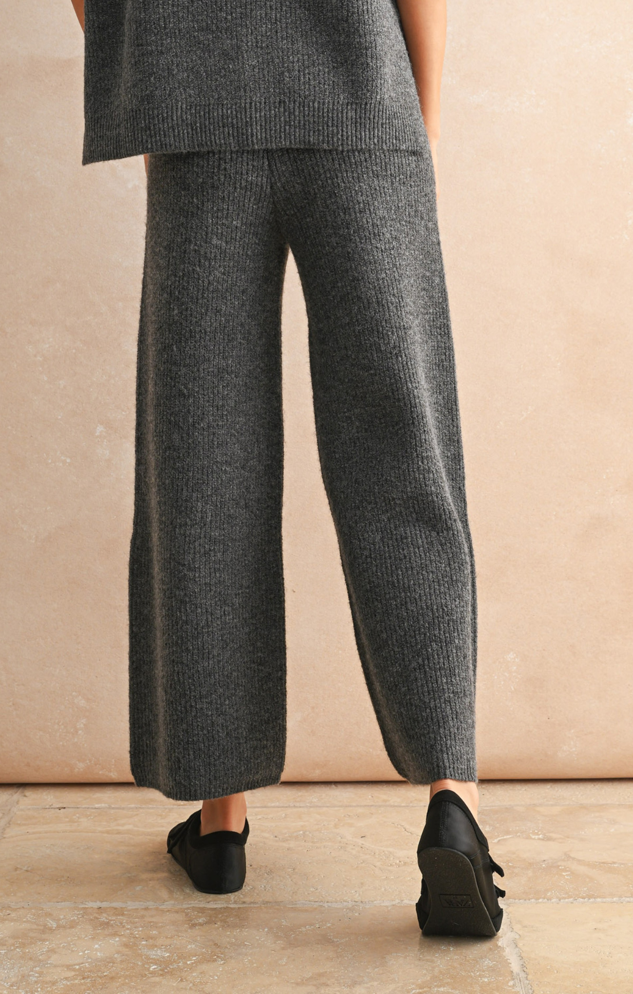 Person wearing gray pants and black shoes on a beige background