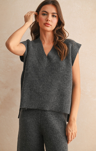 Woman wearing a gray sleeveless top and pants against a beige background