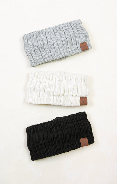 Three knitted headbands in gray, white, and black with brown leather patches on a white background.