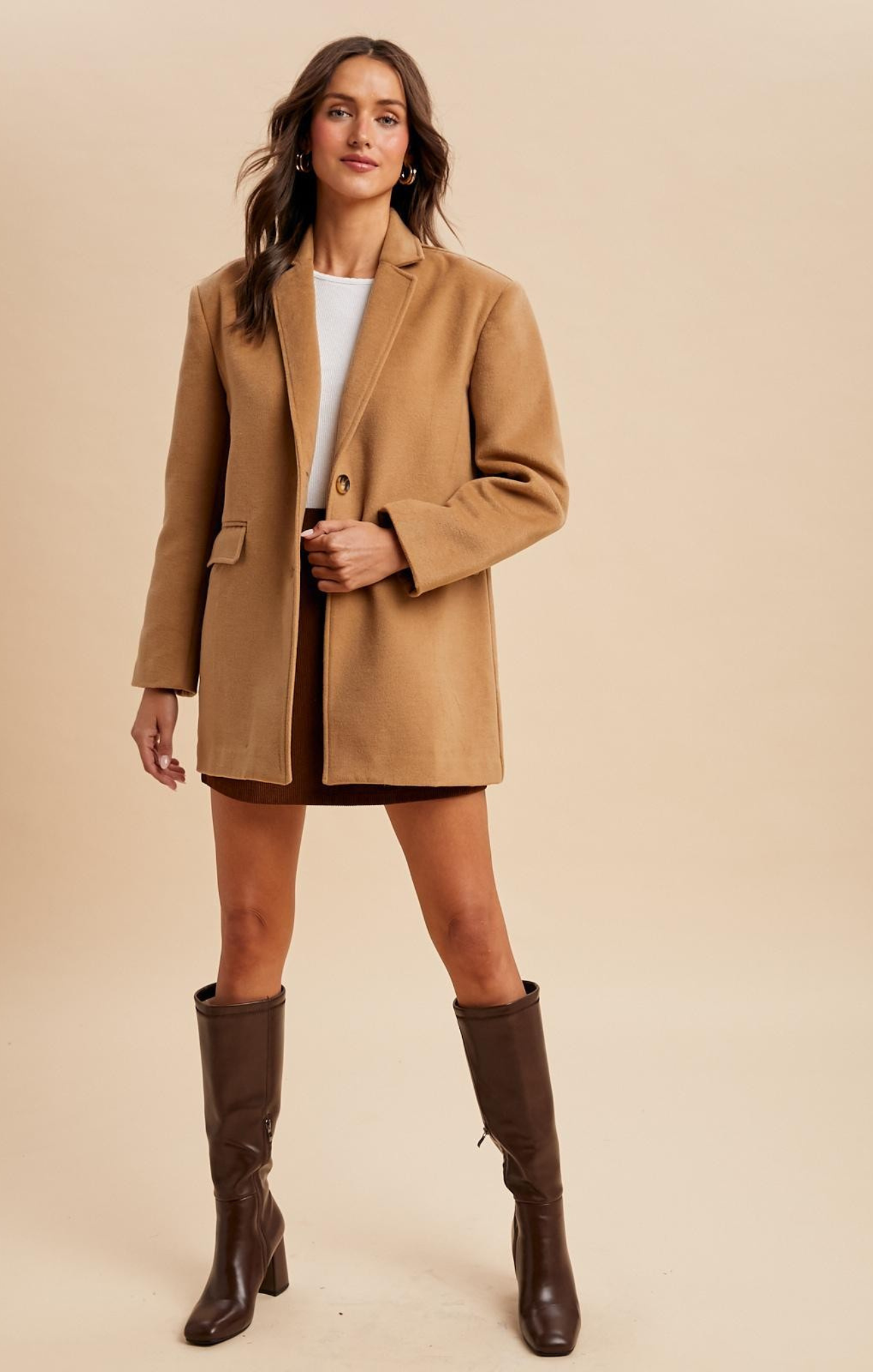 Woman wearing a tan coat and brown knee-high boots on a beige background
