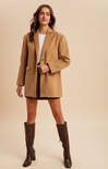 Woman wearing a tan coat and brown knee-high boots on a beige background