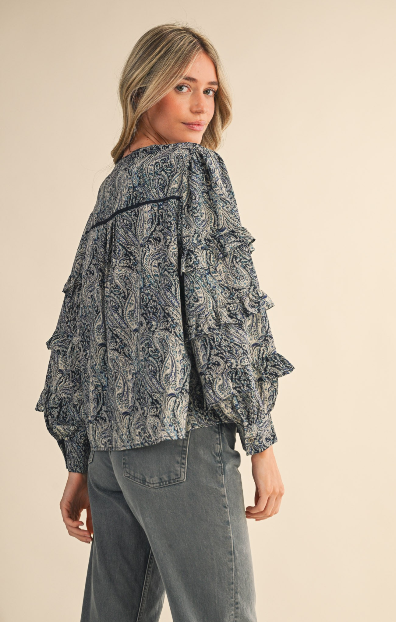 Woman wearing a patterned jacket and gray pants on a beige background