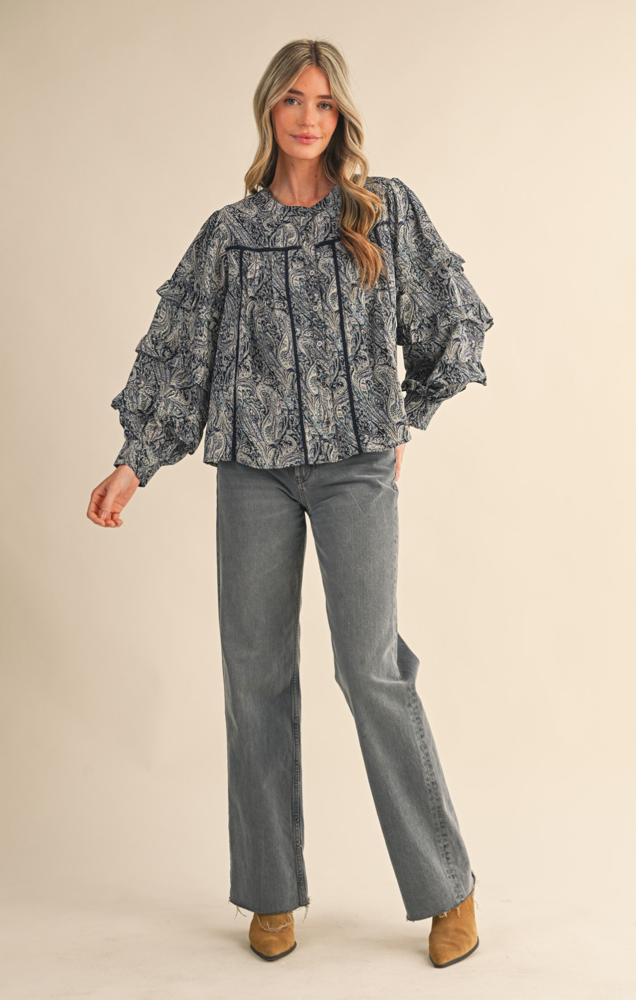 Woman wearing a patterned blouse and gray pants on a beige background