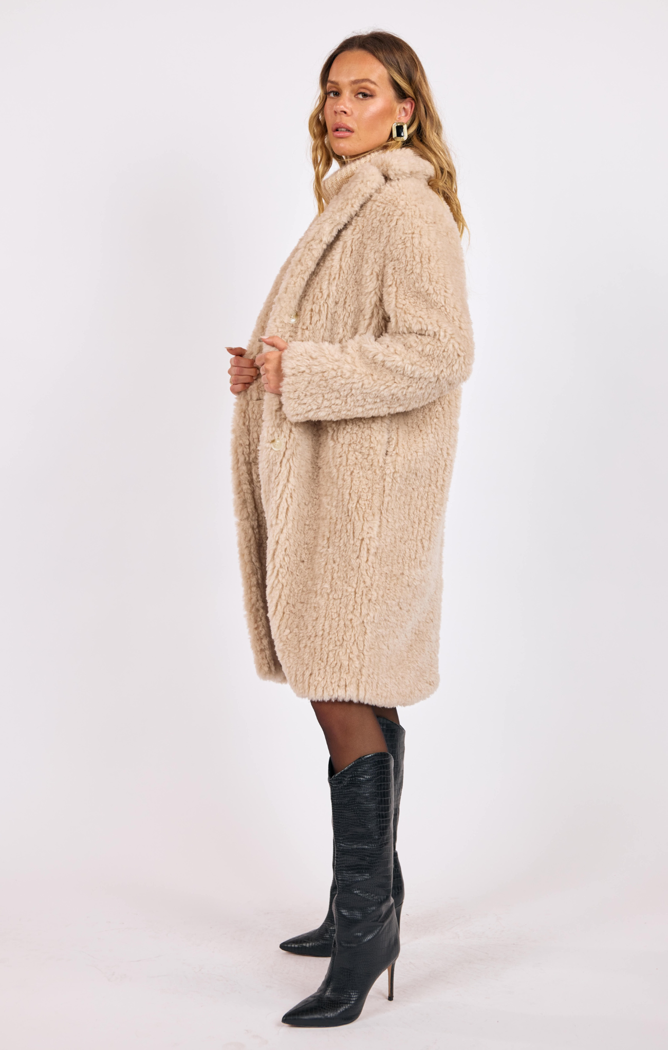 Woman wearing a beige knitted coat and black boots on a white background
