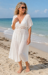 Woman in a white dress standing on a beach with ocean in the background