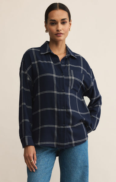 Woman wearing a navy plaid shirt and blue jeans against a beige background
