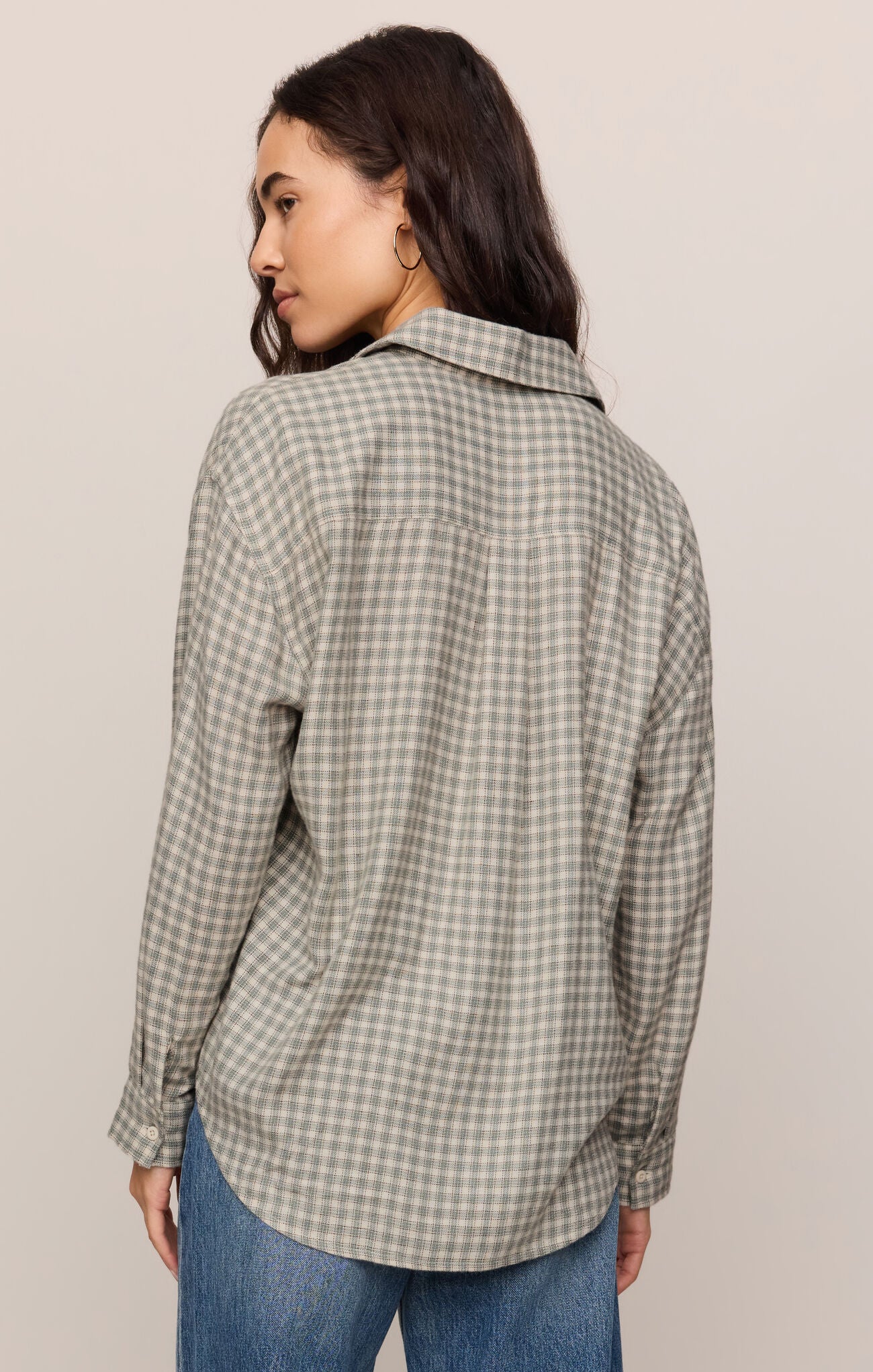 Woman wearing a plaid shirt and jeans against a plain background