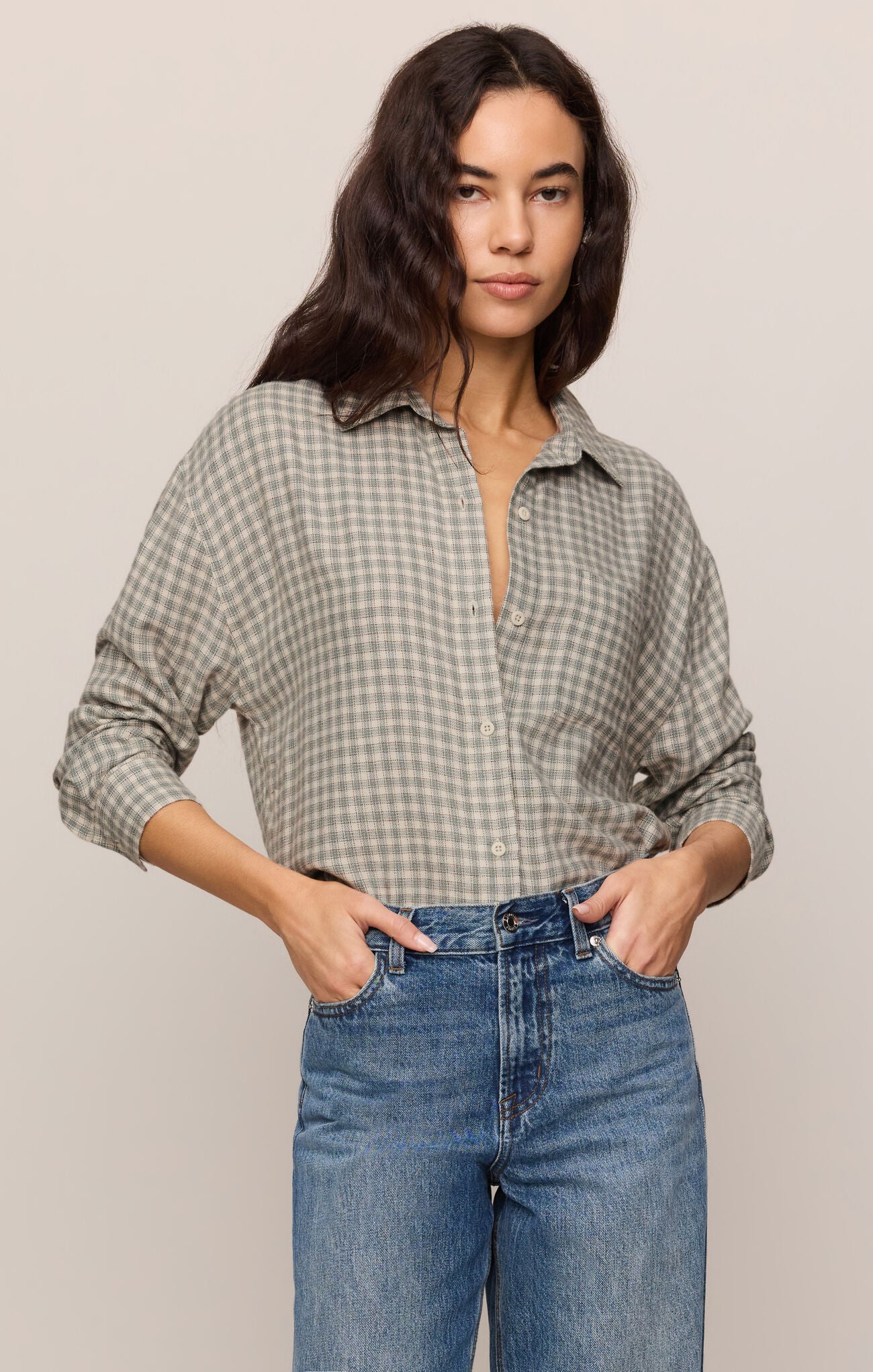 Woman wearing a plaid shirt and jeans against a plain background