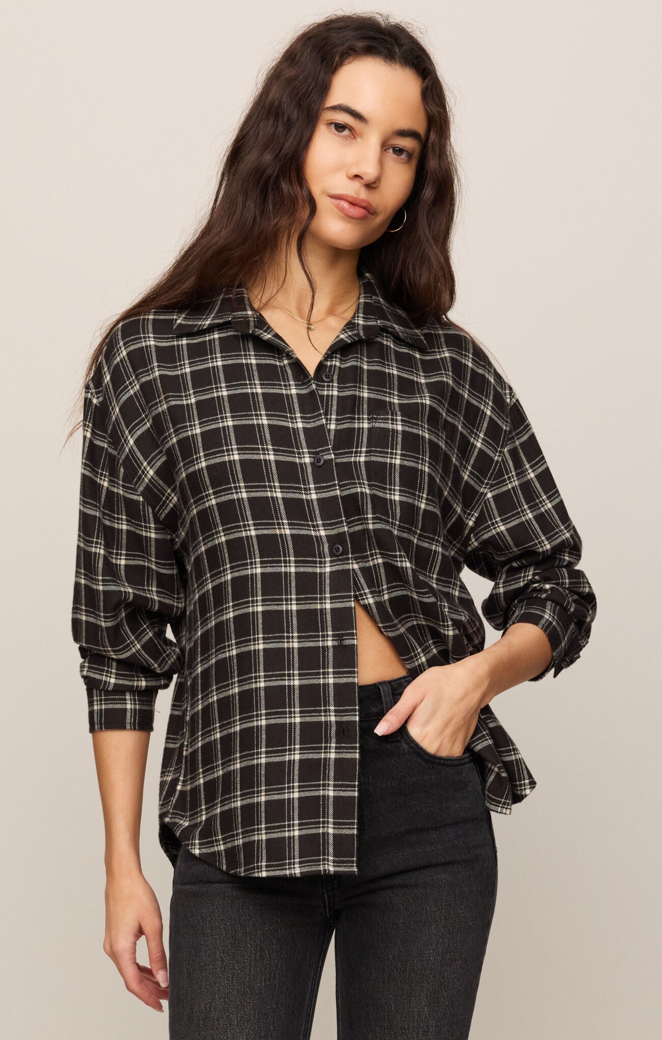 Woman wearing a plaid shirt and black pants against a plain background