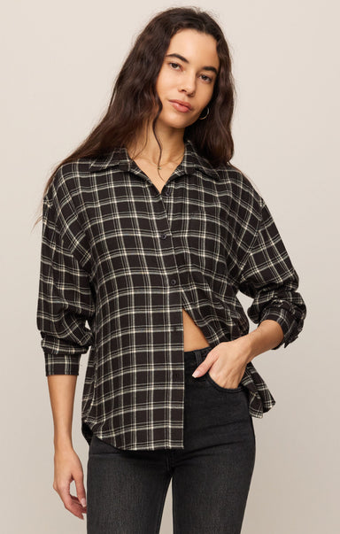 Woman wearing a plaid shirt and black pants against a plain background