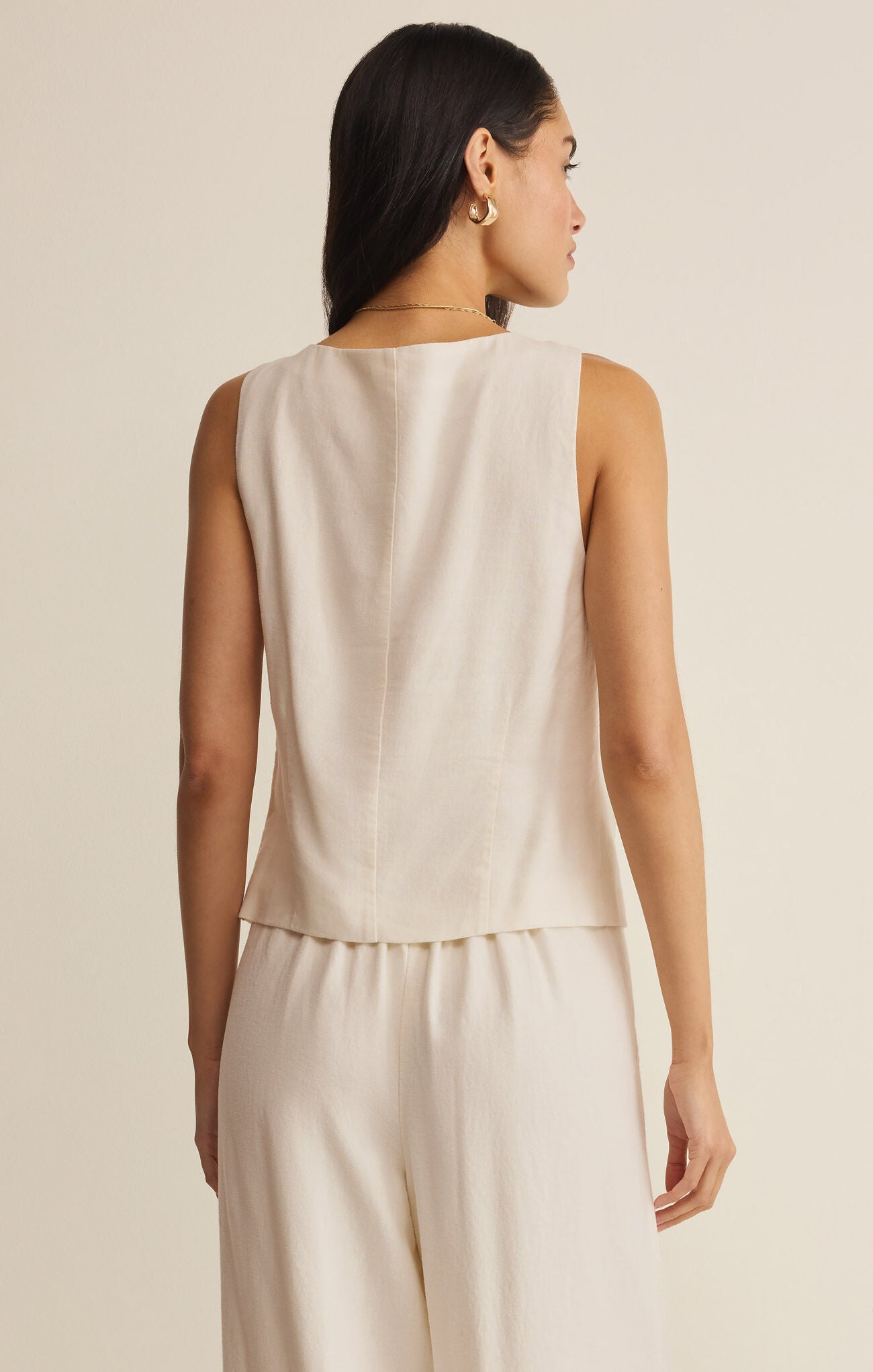 Woman wearing a beige sleeveless top and pants against a neutral background