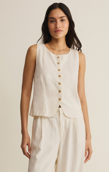 Woman wearing a sleeveless beige top with gold buttons on a plain background