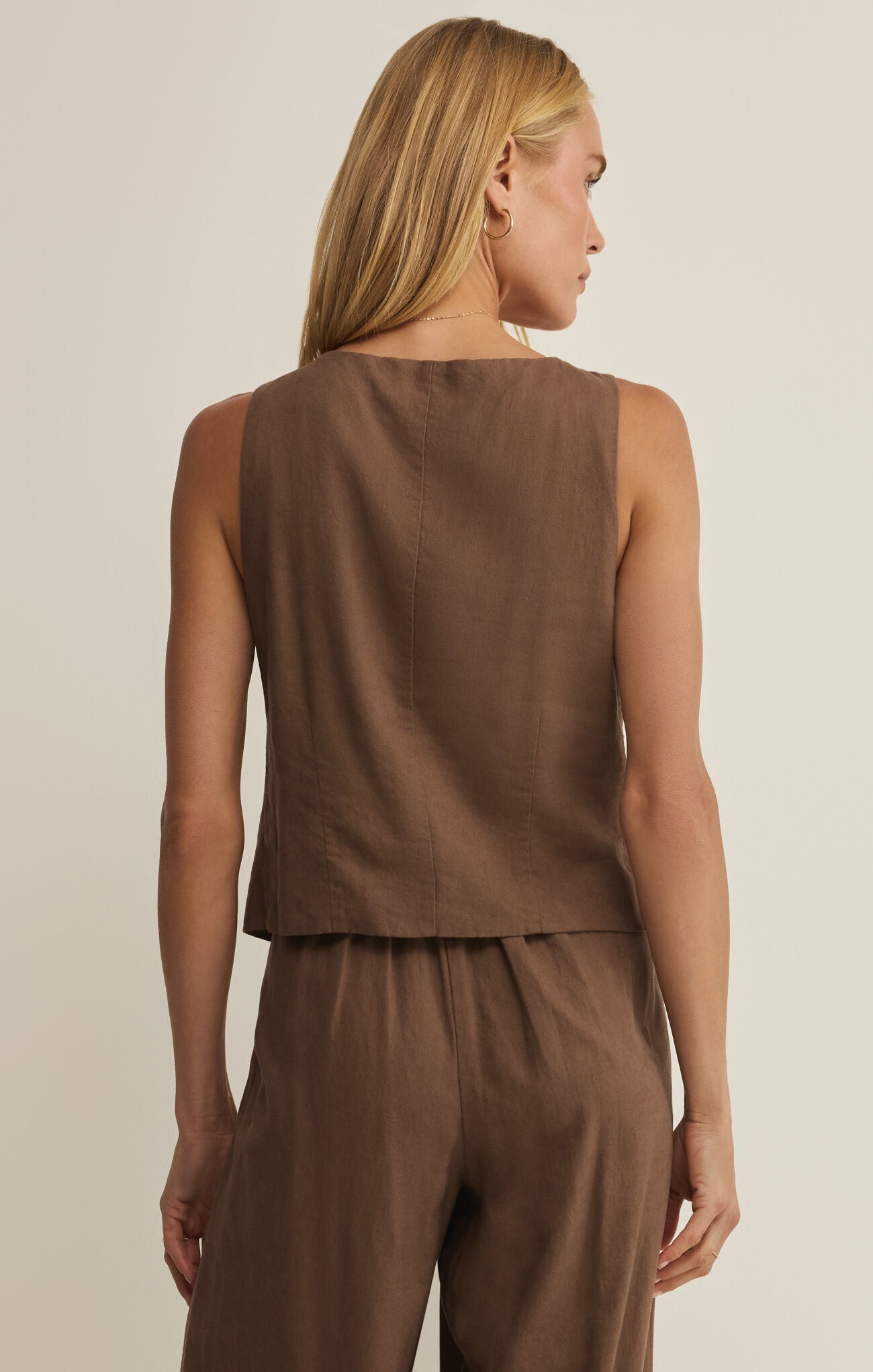 Woman wearing a brown sleeveless top and pants against a beige background