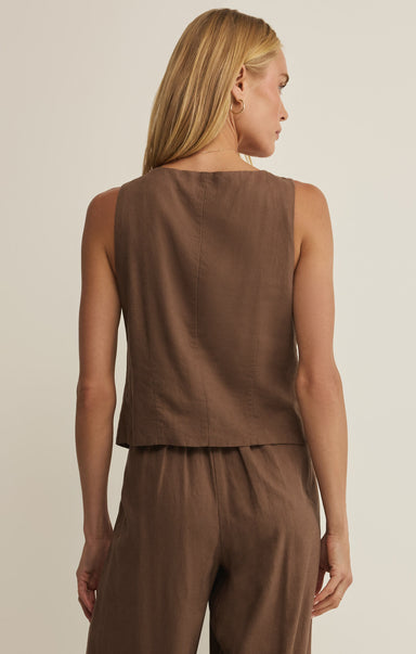 Woman wearing a brown sleeveless top and pants against a beige background