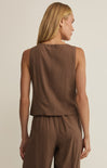 Woman wearing a brown sleeveless top and pants against a beige background
