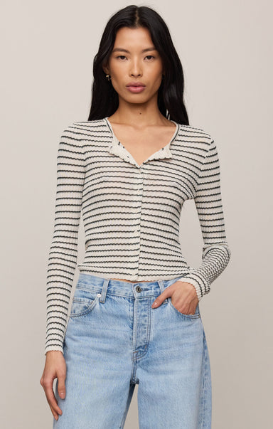 Woman wearing a striped long-sleeve top and blue jeans against a plain background