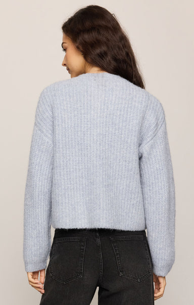 Person wearing a light blue textured sweater and dark jeans on a beige background