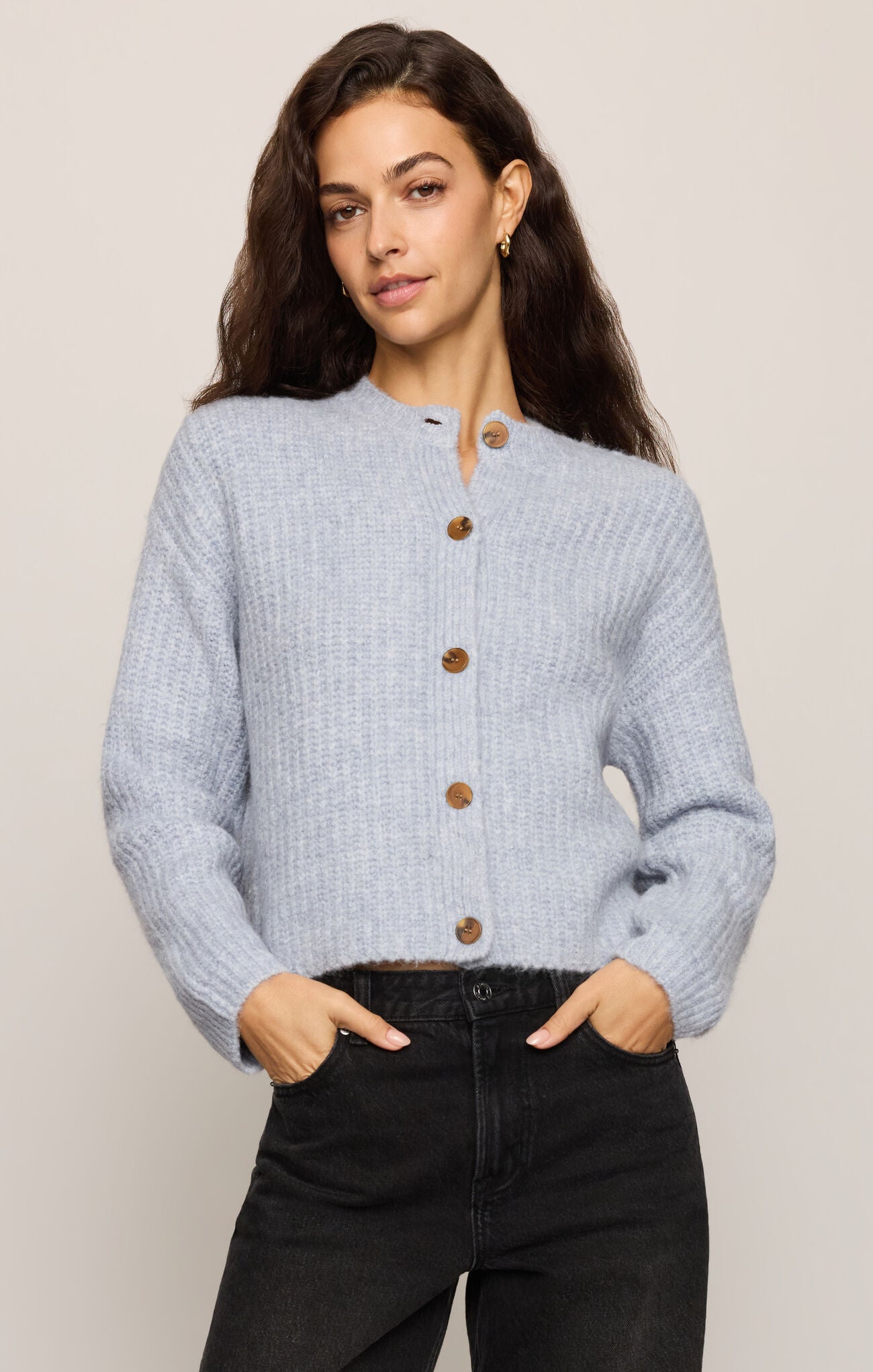 Woman wearing a light blue cardigan with brown buttons on a plain background