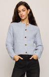 Woman wearing a light blue cardigan with brown buttons on a plain background