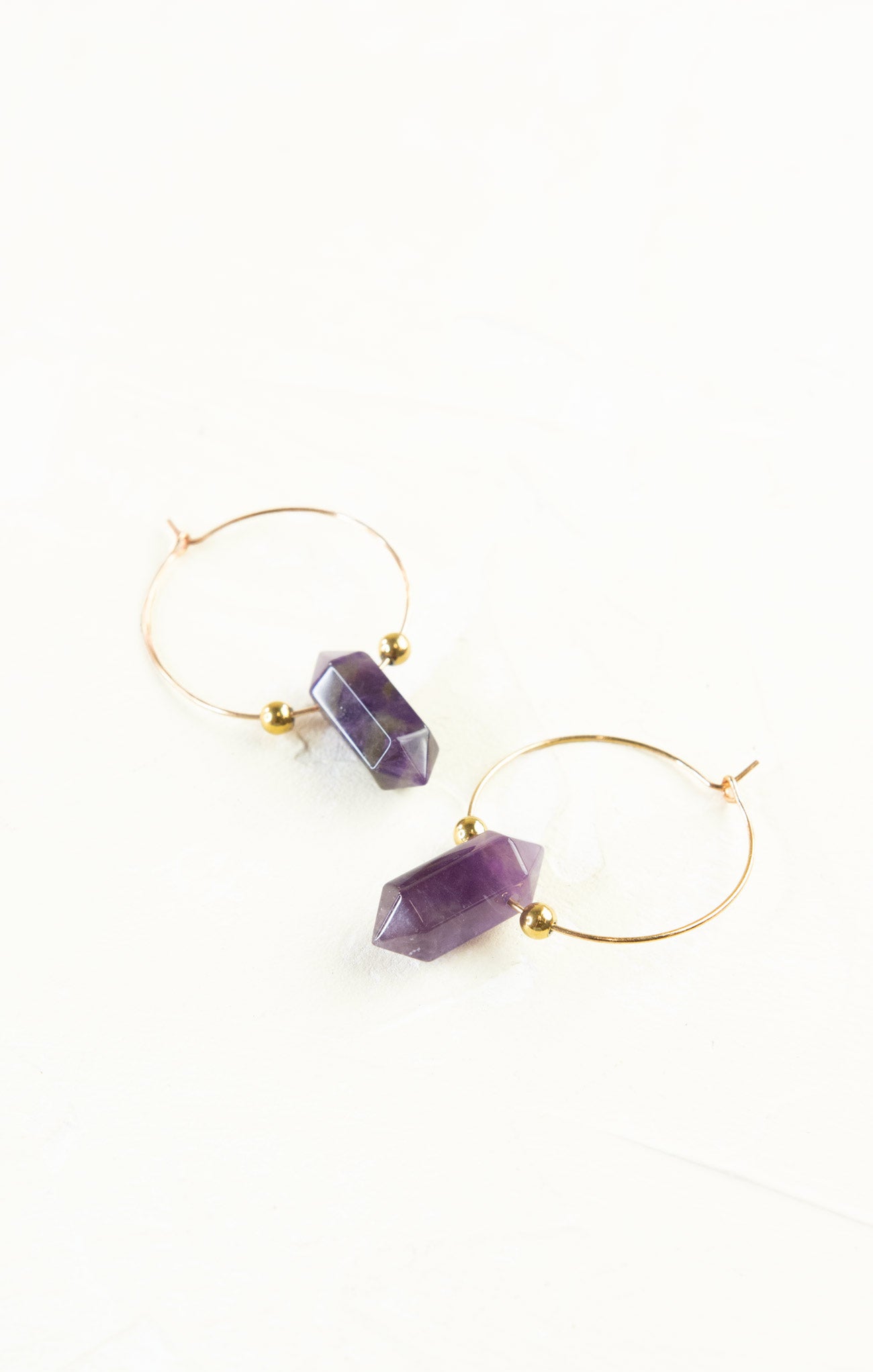 Gold hoop earrings with purple gemstone drops on a white background