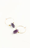 Gold hoop earrings with purple gemstone drops on a white background