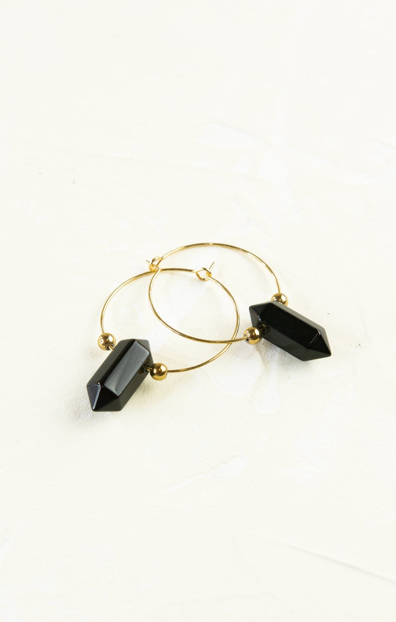 Gold hoop earrings with black geometric beads on a white background