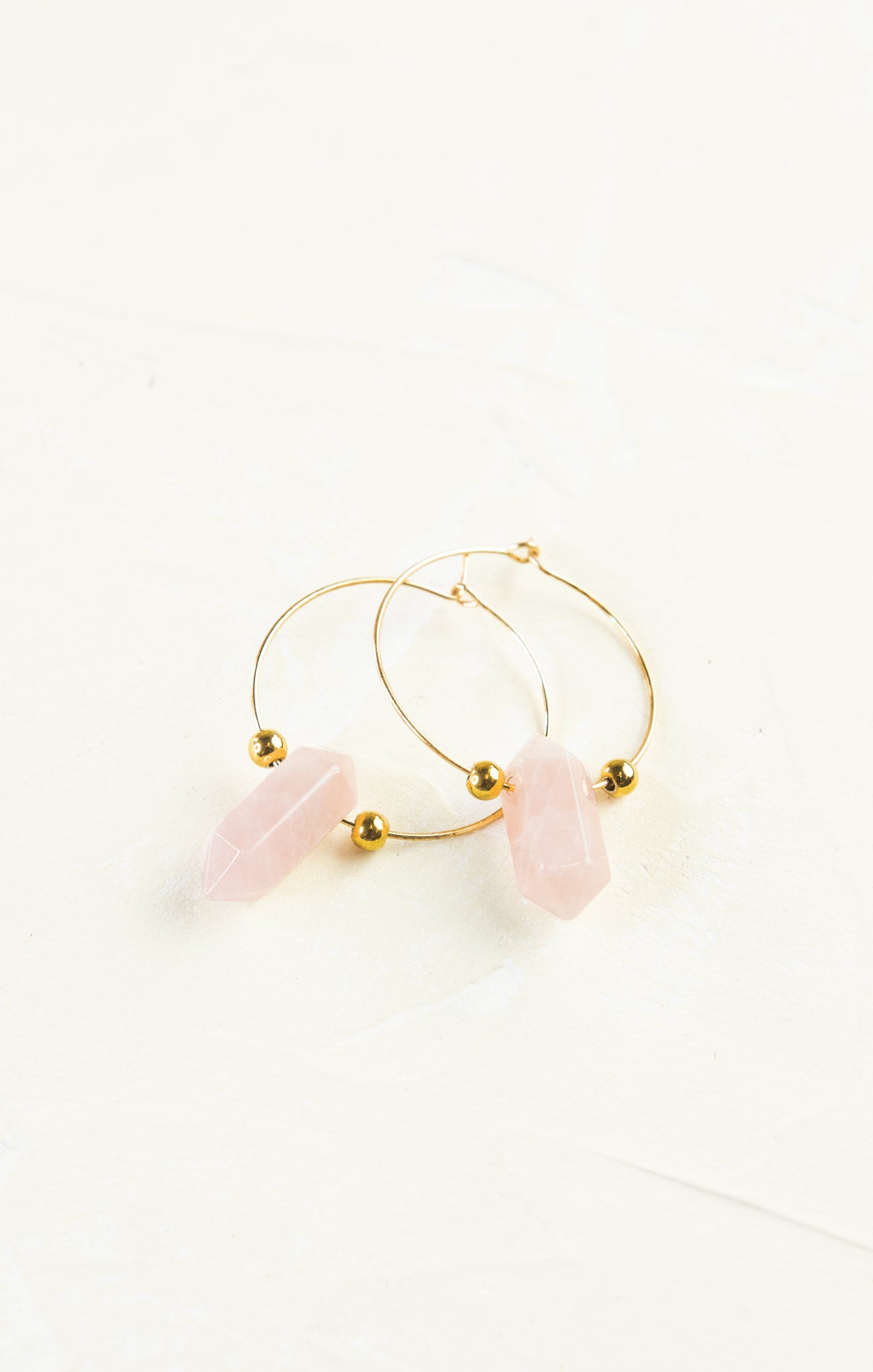 Gold hoop earrings with pink stones on a white background