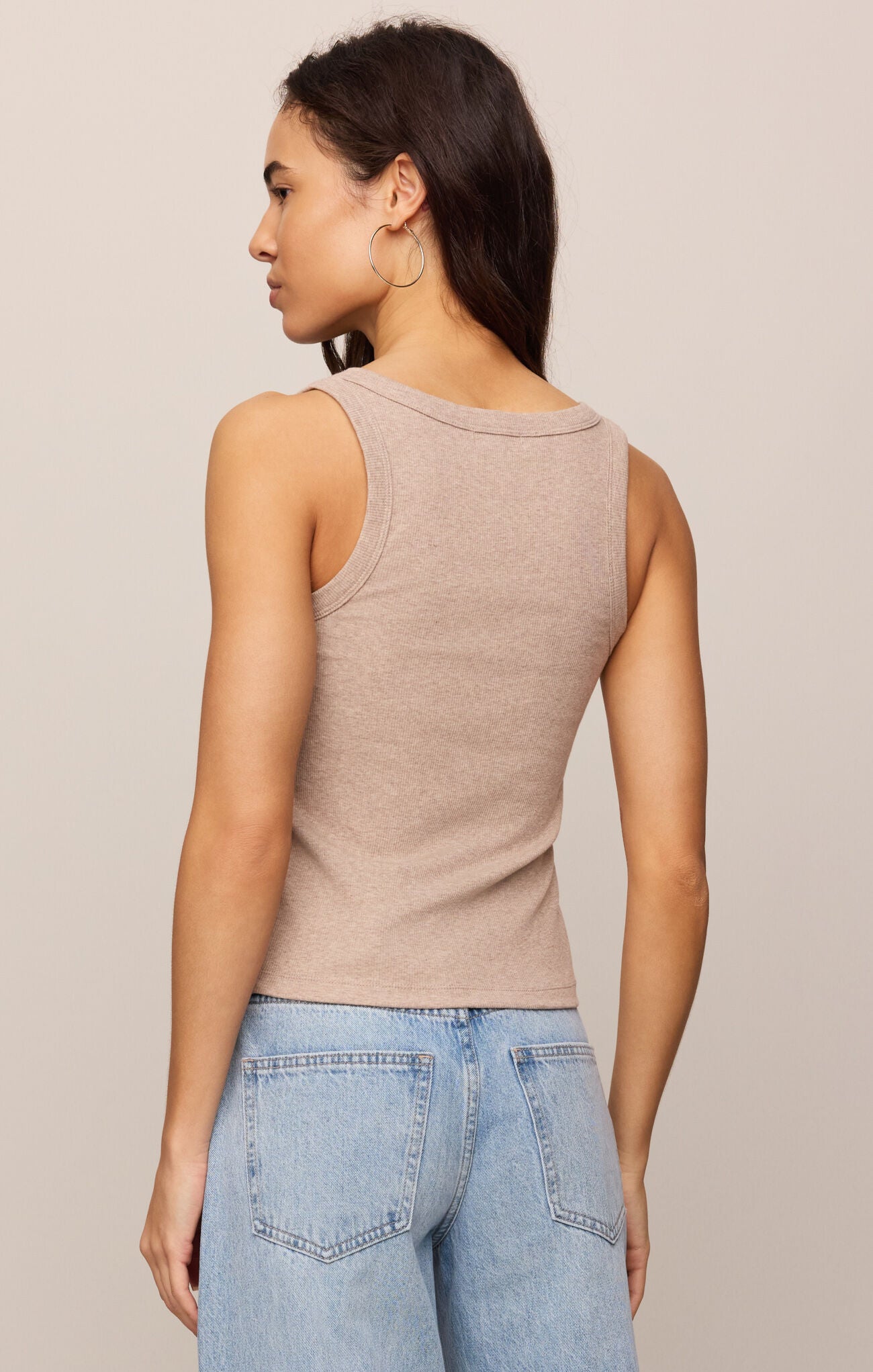 Woman wearing a beige tank top and light blue jeans against a neutral background