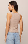 Woman wearing a beige tank top and light blue jeans against a neutral background
