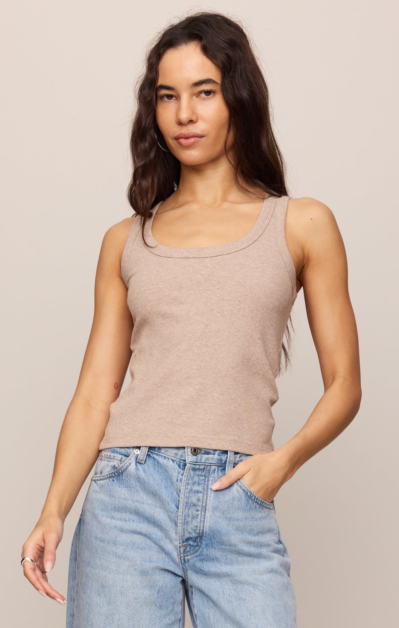 Woman wearing a beige tank top and blue jeans against a plain background