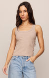 Woman wearing a beige tank top and blue jeans against a plain background