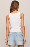 Woman wearing a white sleeveless top and light blue denim shorts on a beige background