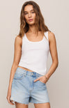 Woman wearing a white tank top and denim shorts on a plain background