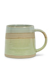 A handmade ceramic mug with a wide handle, featuring a horizontal band of matte beige glaze over a glossy light green body, set against a plain white background.