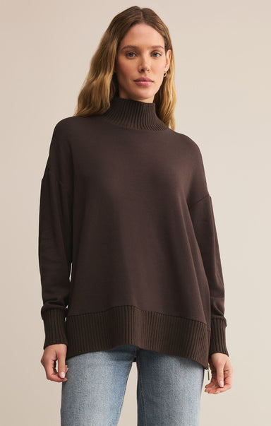 Woman wearing a brown turtleneck sweater and light blue jeans on a beige background