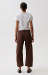 A model shown from the back wearing brown wide-leg cropped trousers, a white t-shirt, and black shoes against a plain light gray background.
