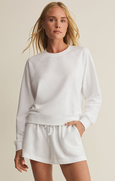 Woman wearing a white sweatshirt and shorts set against a beige background