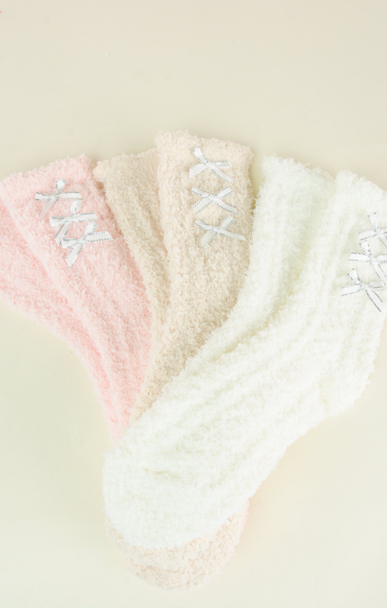 Three pairs of fuzzy socks in pink, white, and beige with lace details on a light background.