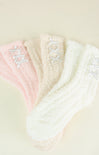 Three pairs of fuzzy socks in pink, white, and beige with lace details on a light background.