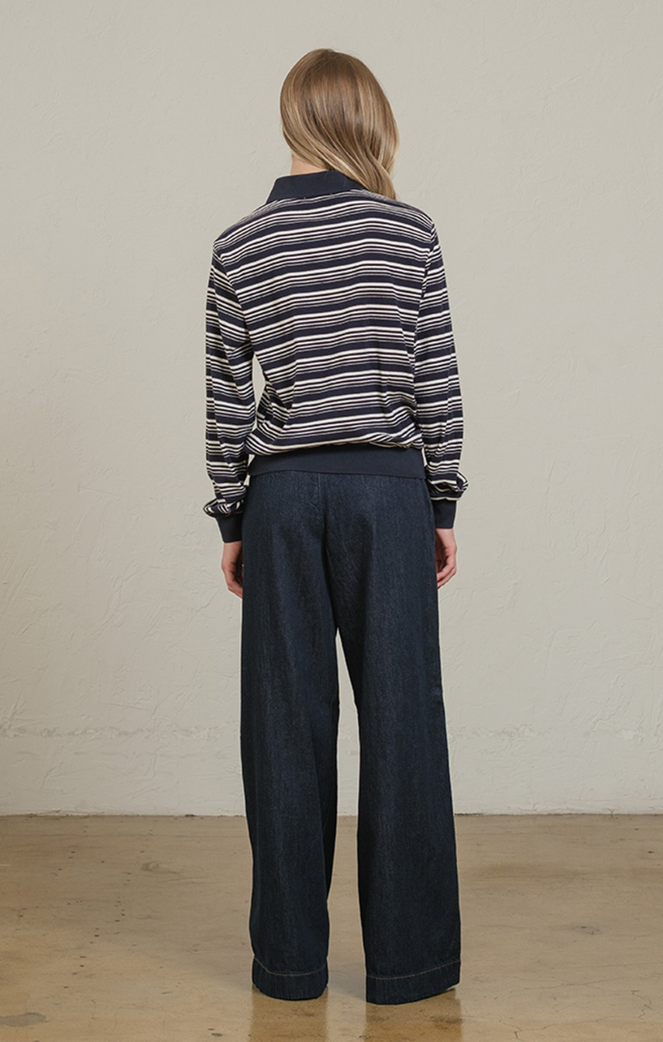 Person wearing a striped sweater and dark pants against a plain background