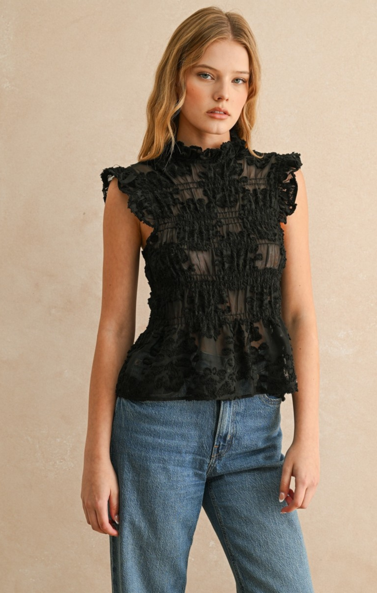 Woman wearing a black ruffled top and blue jeans against a beige background