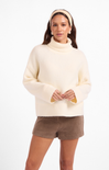 Woman wearing a cream sweater and brown shorts on a white background