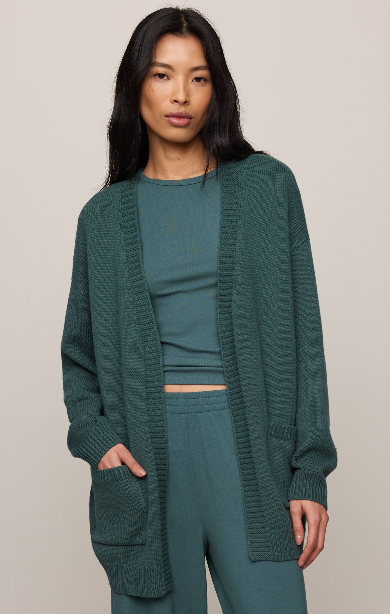 Woman wearing a green outfit with a matching cardigan on a beige background