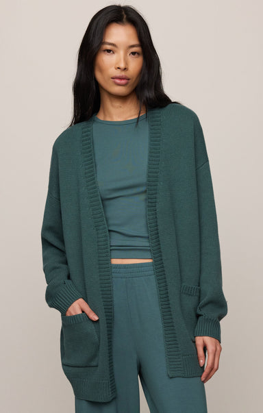 Woman wearing a green outfit with a matching cardigan on a beige background