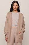 Woman wearing a beige cardigan over a light gray top and beige pants on a plain background